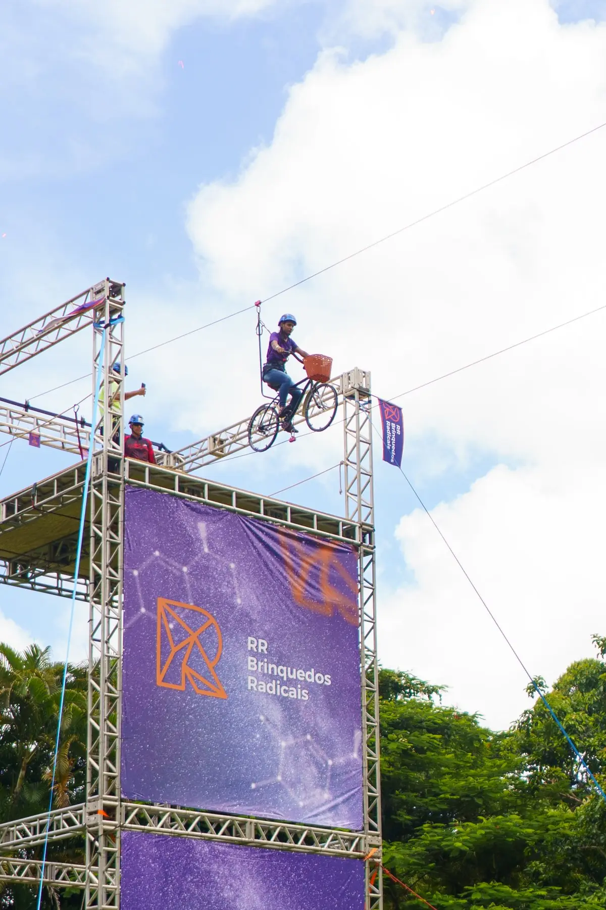 Operador pedalando a Sky Bike com a bandeira RR Brinquedos Radicais, sobre estrutura de truss